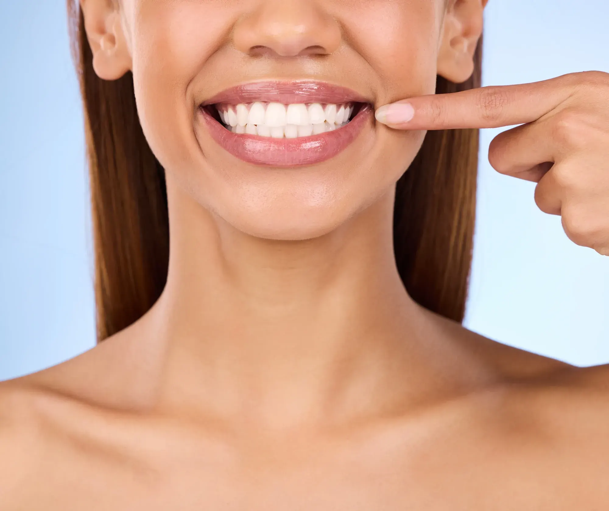 Smiling woman pointing to her even teeth and balanced gumline after gummy smile treatment in NYC