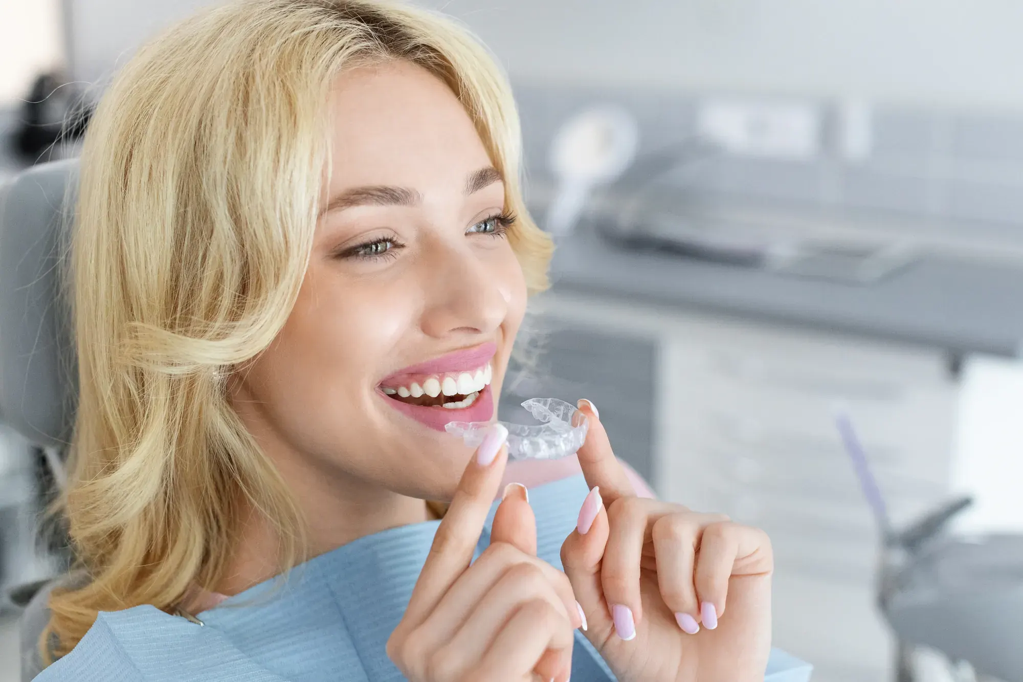 Woman in a dental chair holding up her new Invisalign clear aligner during a fitting at an NYC dental office