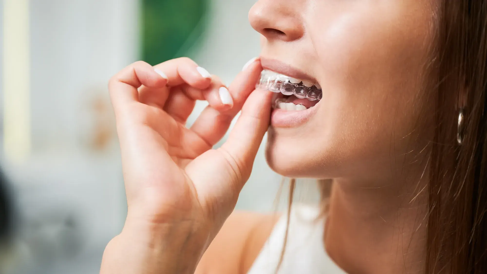 Woman with traditional metal braces adjusting an elastic, a comparison point for Invisalign vs. braces