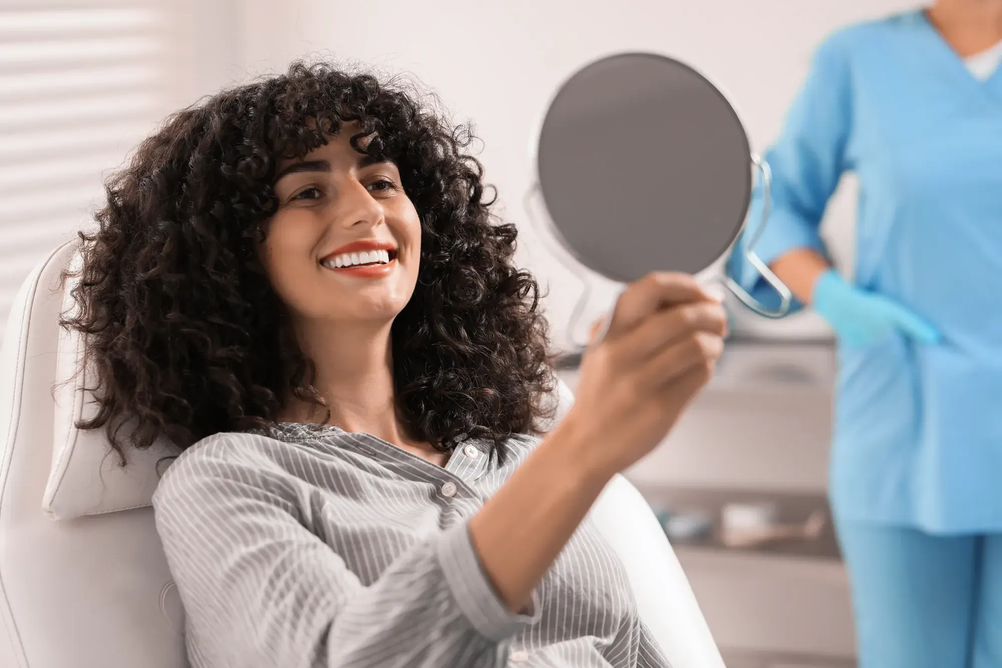 Woman in a dental chair admiring her new smile in a hand mirror after a smile makeover at a Tribeca dental office