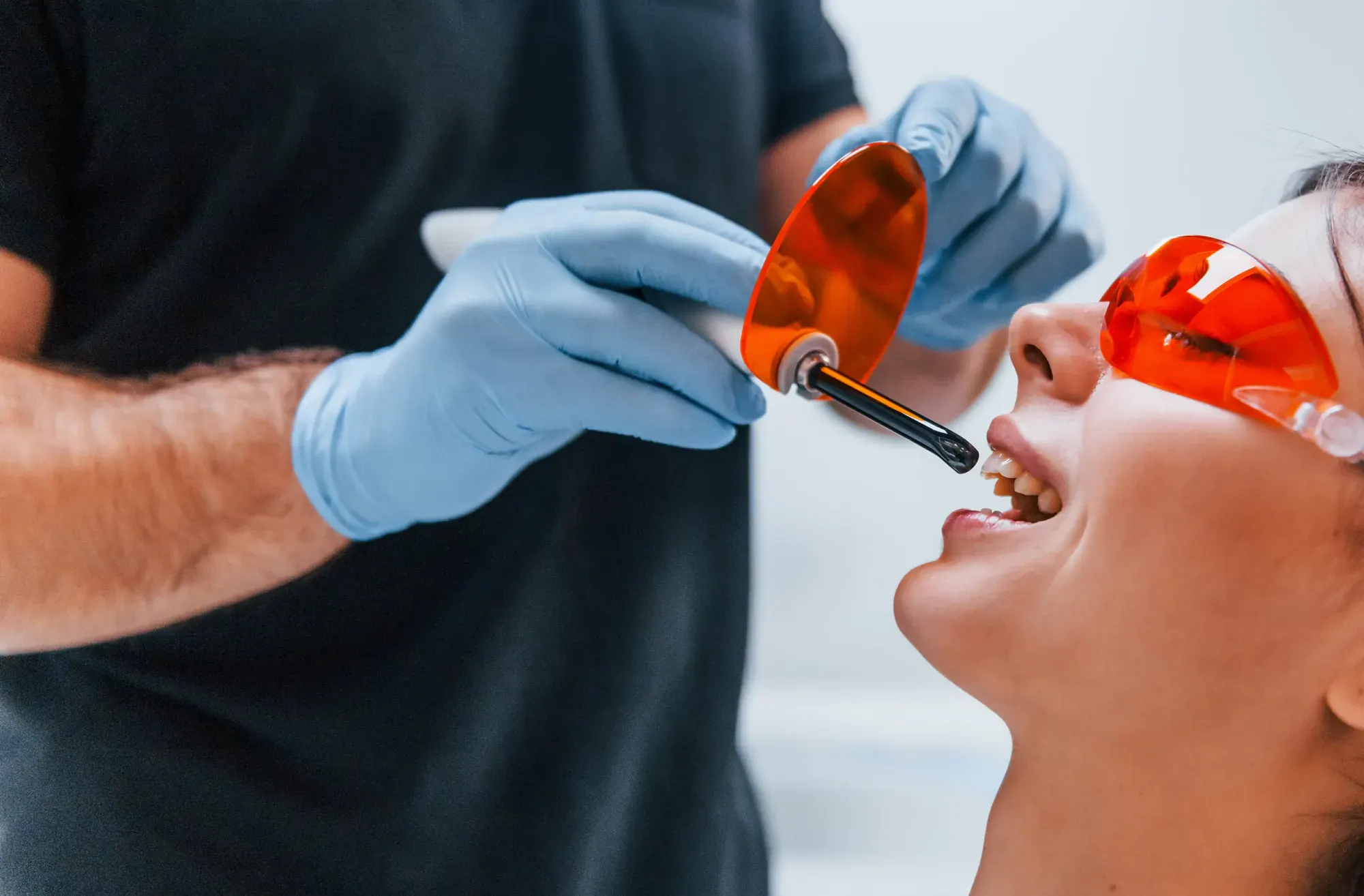 Dentist using a curing light to harden tooth-colored bonding resin while the patient wears orange safety glasses