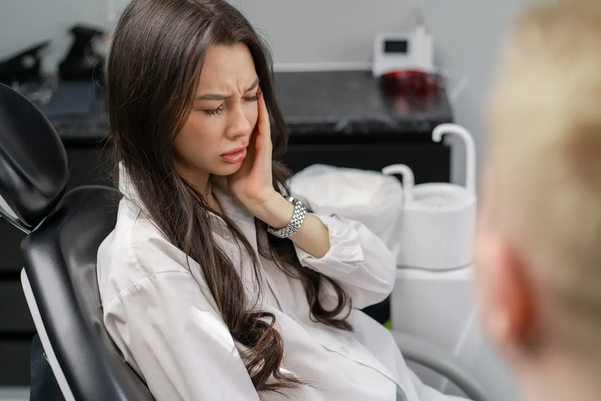 Woman in a dental chair holding her cheek from tooth pain during a same-day emergency visit in NYC