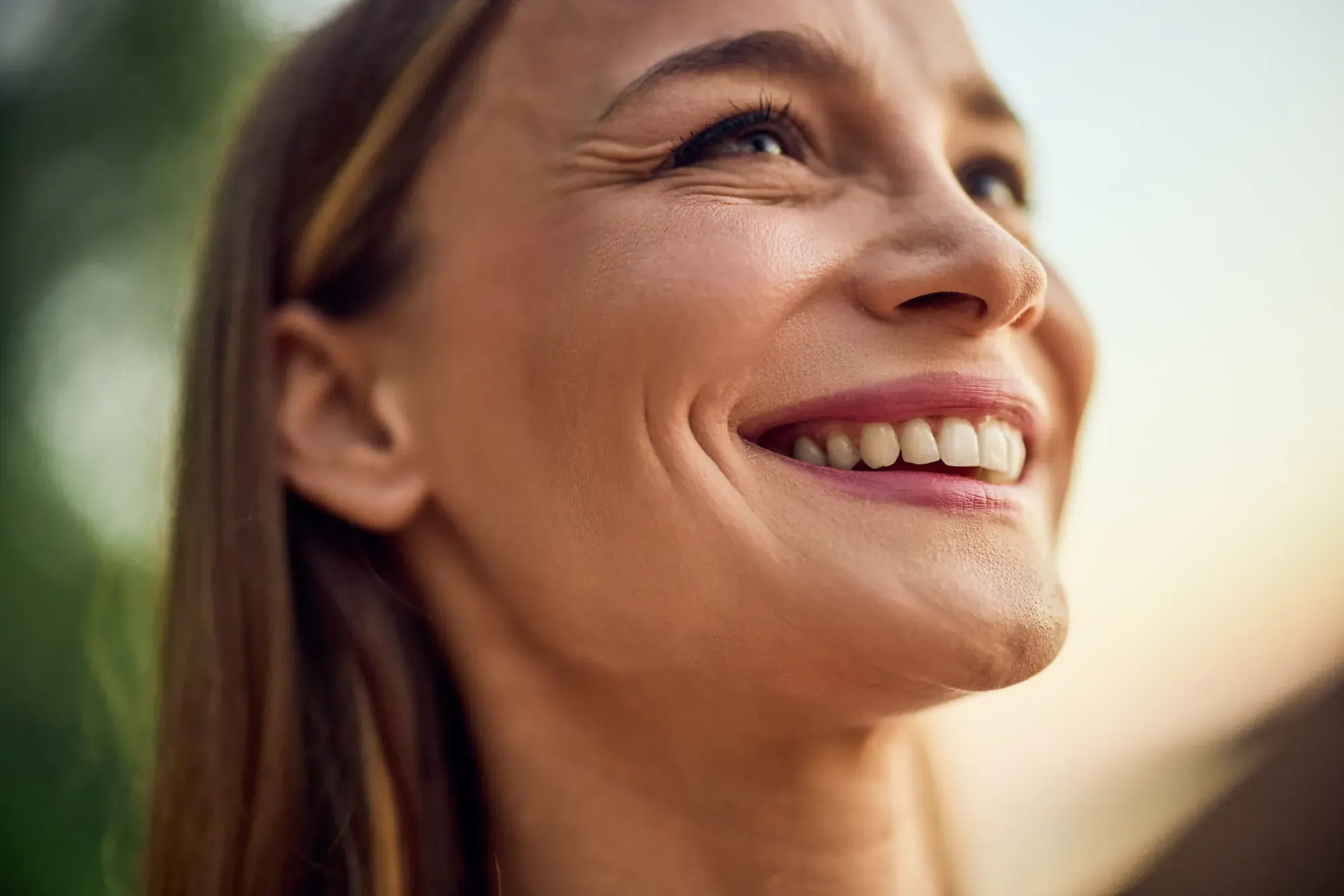 Mature woman smiling in warm sunlight with a full, youthful lower face, the goal of the Smile Facelift® in NYC