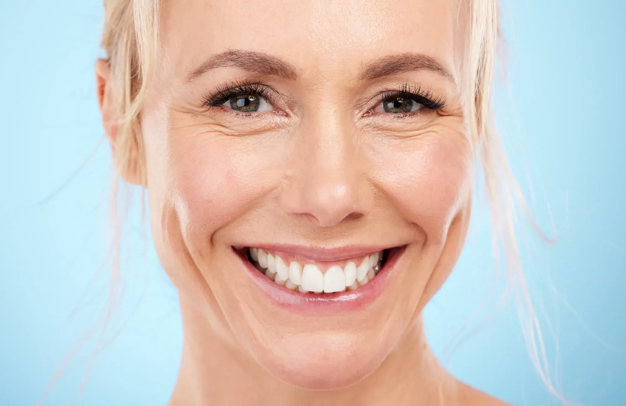 Smiling mature woman with bright teeth on a light blue background, illustrating non-surgical smile rejuvenation in Tribeca