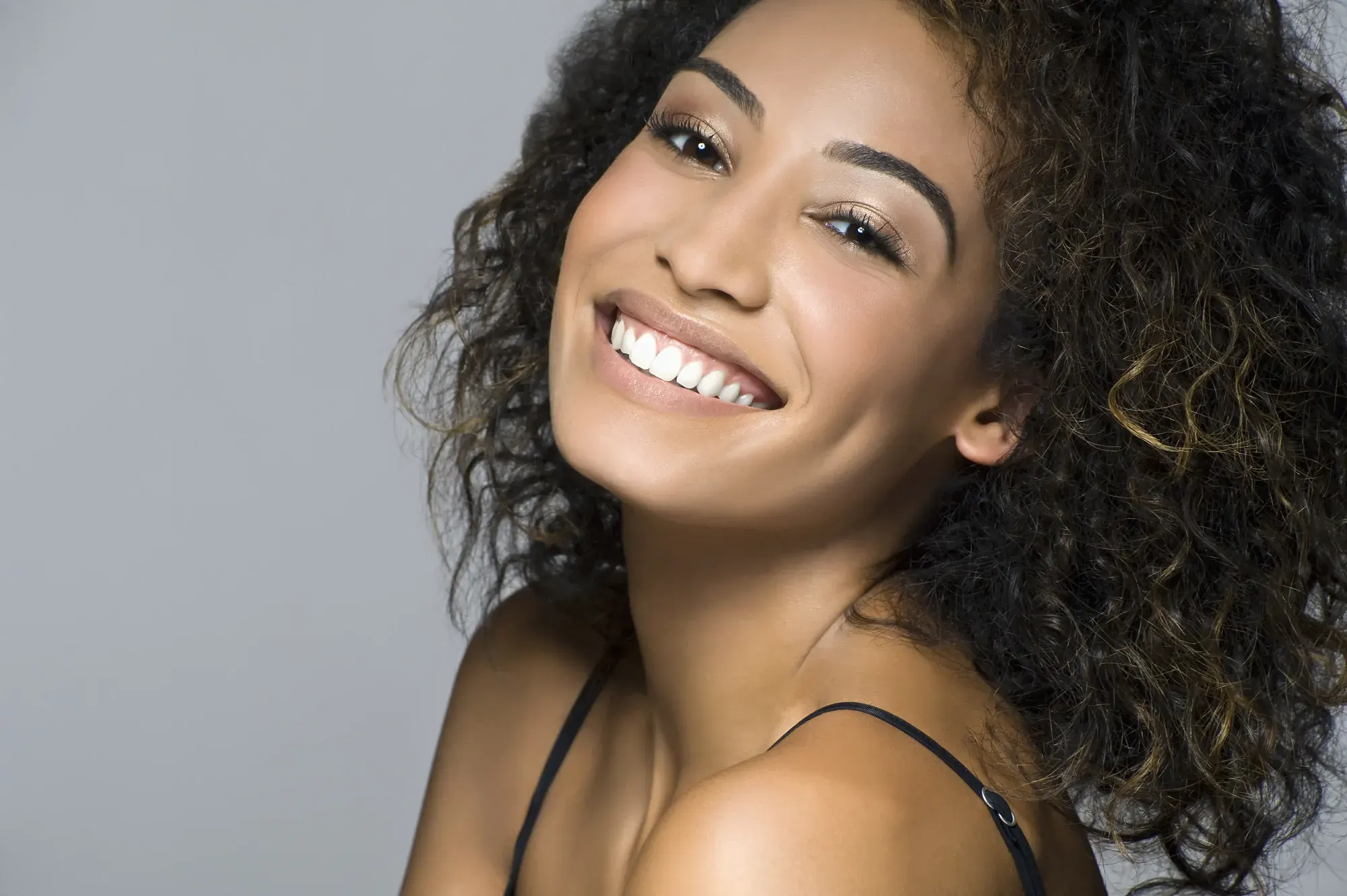 Portrait of a confident woman with curly hair and a radiant smile, the kind of result a smile makeover in NYC aims for
