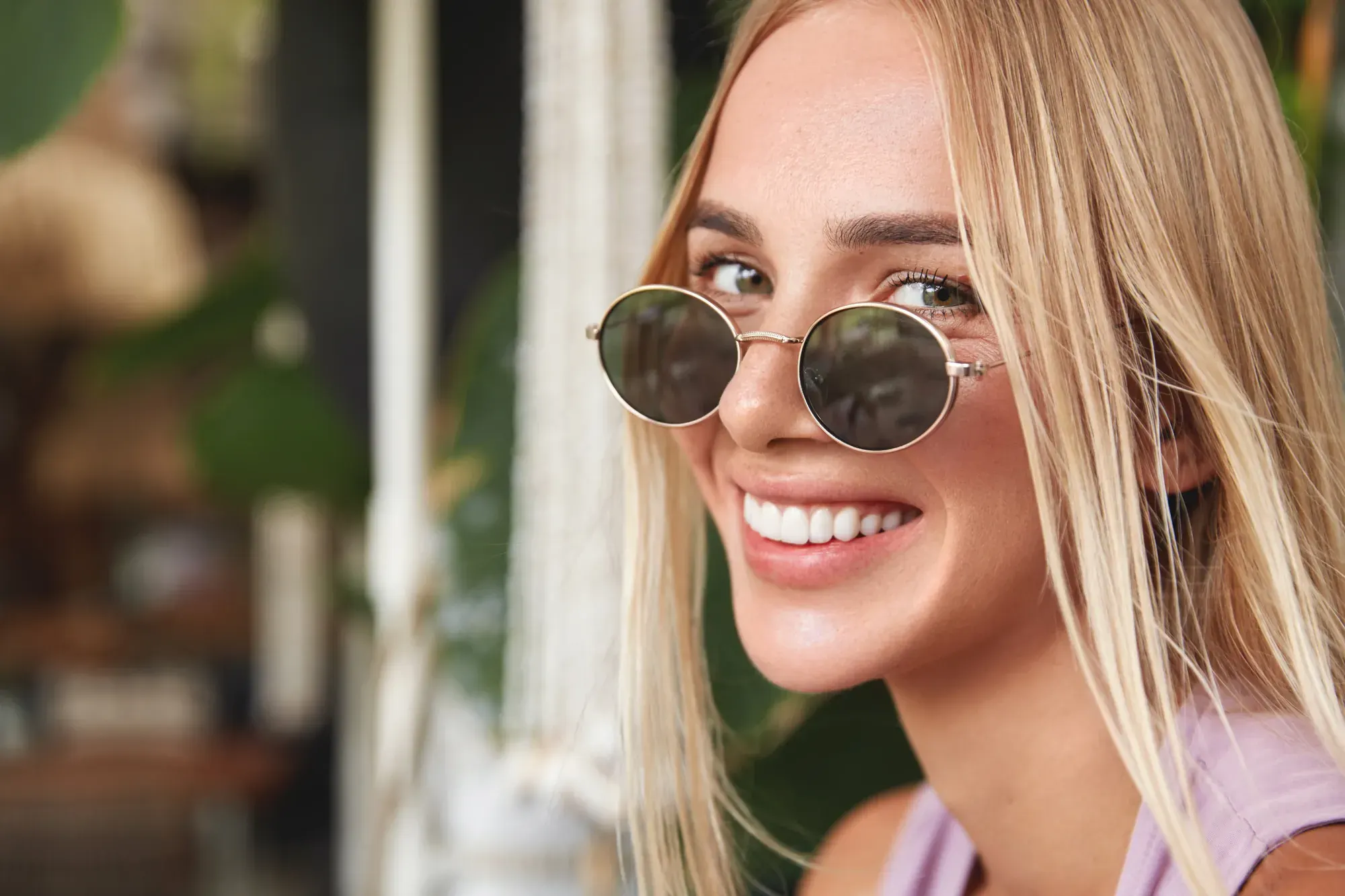 Smiling woman in round sunglasses with a natural, even smile, illustrating smile makeover results in Manhattan