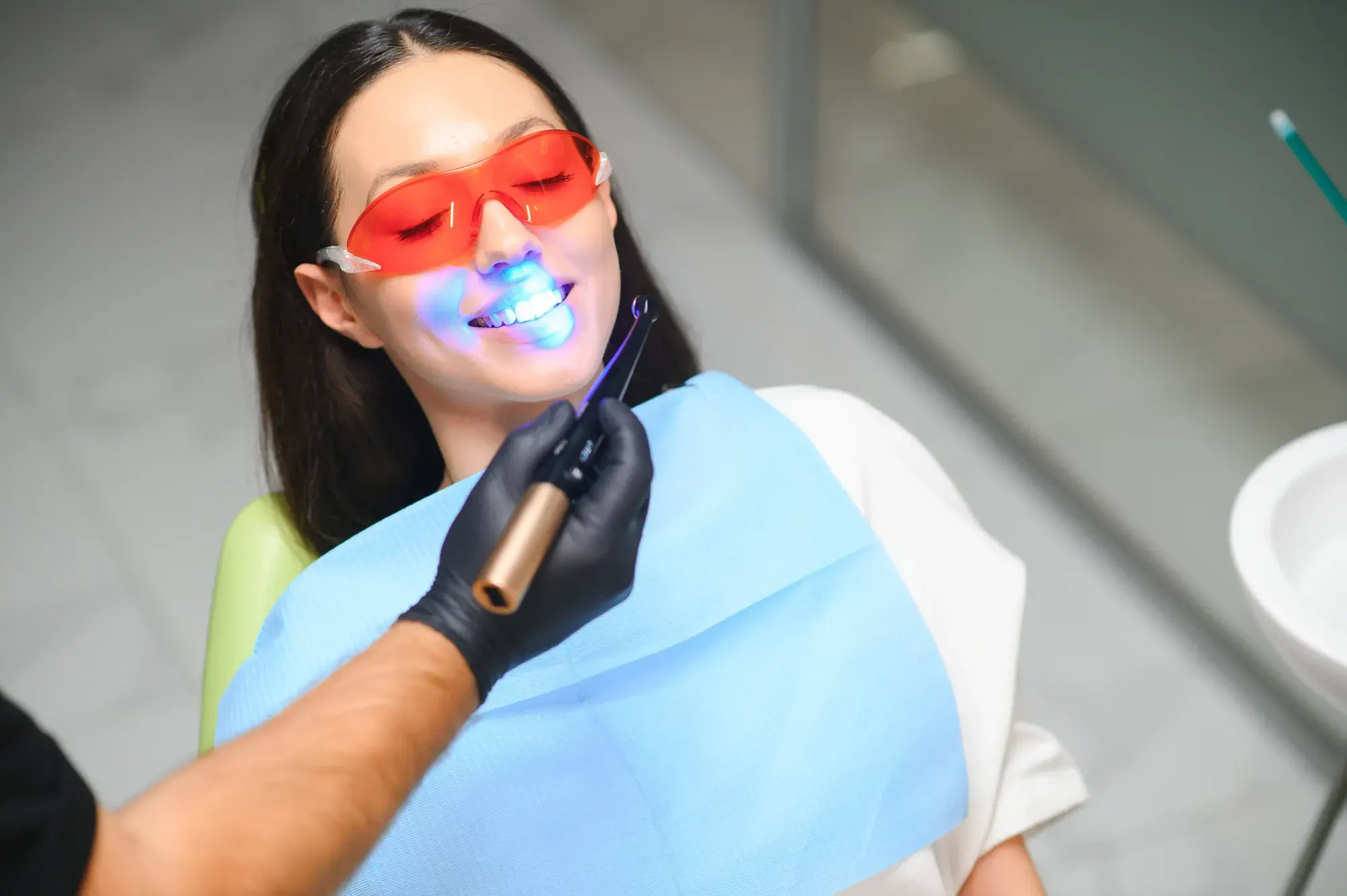 Dentist curing a mercury-free white filling with a blue light while the patient wears protective glasses