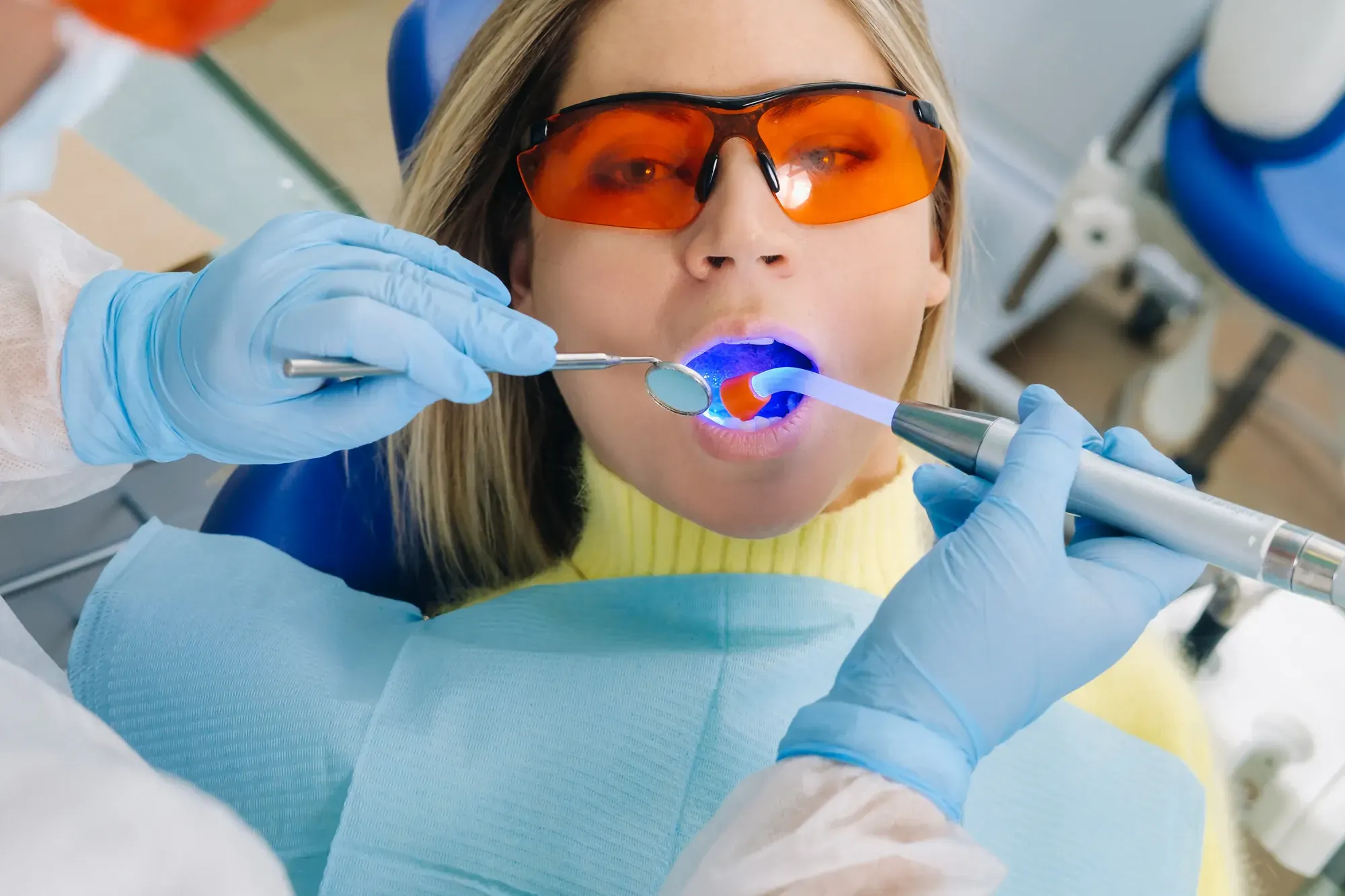 Patient in orange safety glasses as a dentist sets a tooth-colored composite filling with a curing light in Tribeca